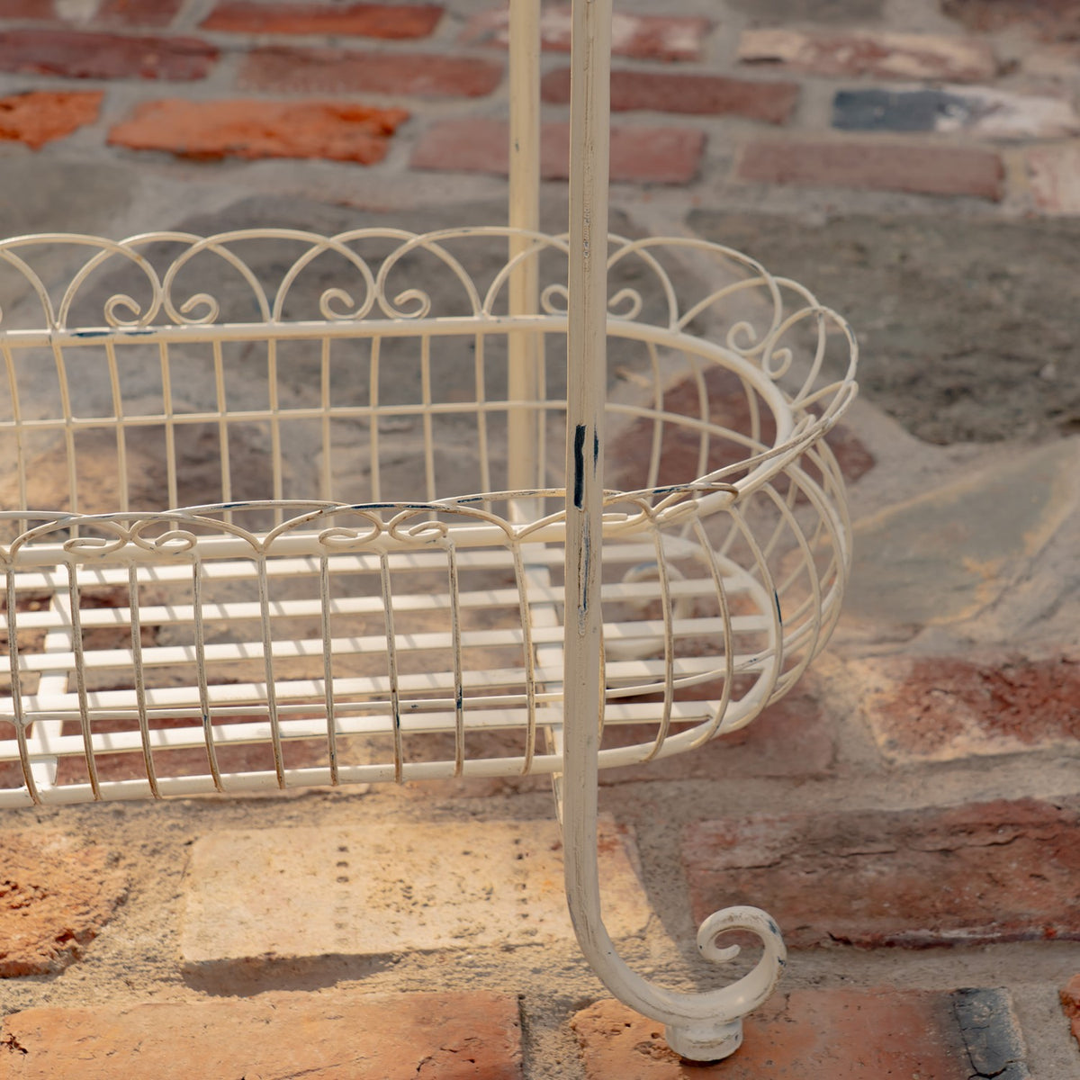 Close view of the stand’s curved wire basket, vertical support, and curled foot against stone paving.
