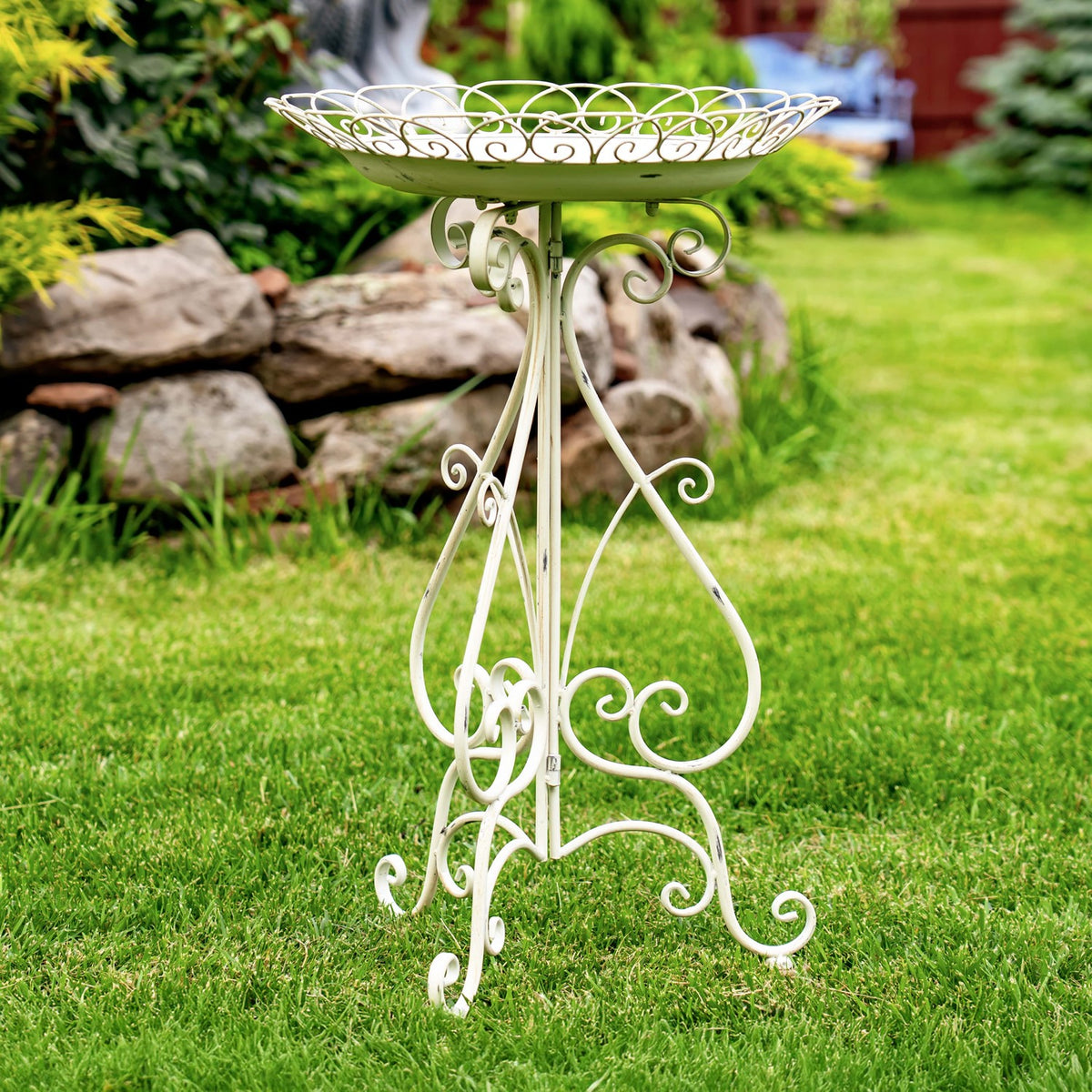 White iron birdbath with an ornate round rim and curled supports, photographed from the side.