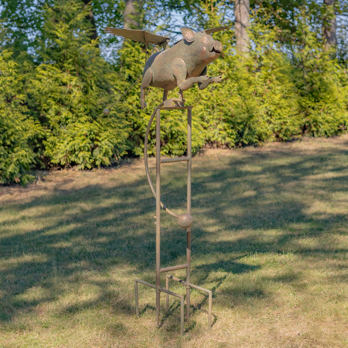 Full view of the winged pig ornament and its tall iron stake standing on a lawn.