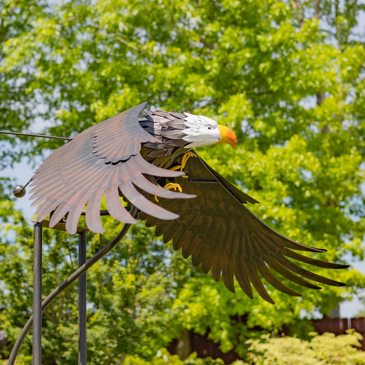 Bald eagle stake with wings extended against a leafy garden backdrop