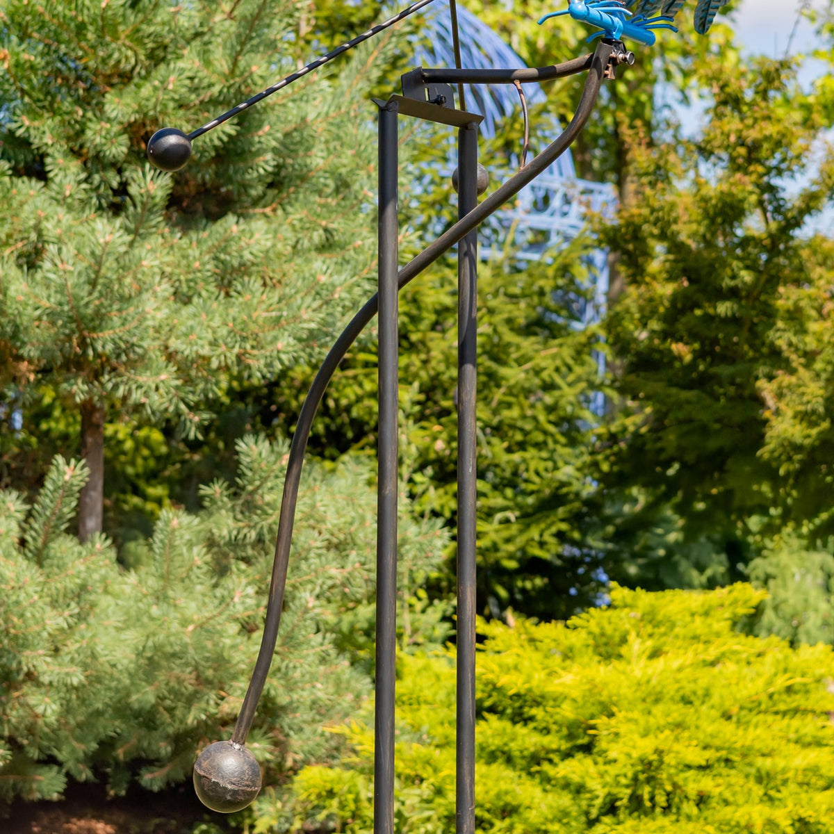 Curved metal supports and weighted arms beneath the bird, shown against garden shrubs.