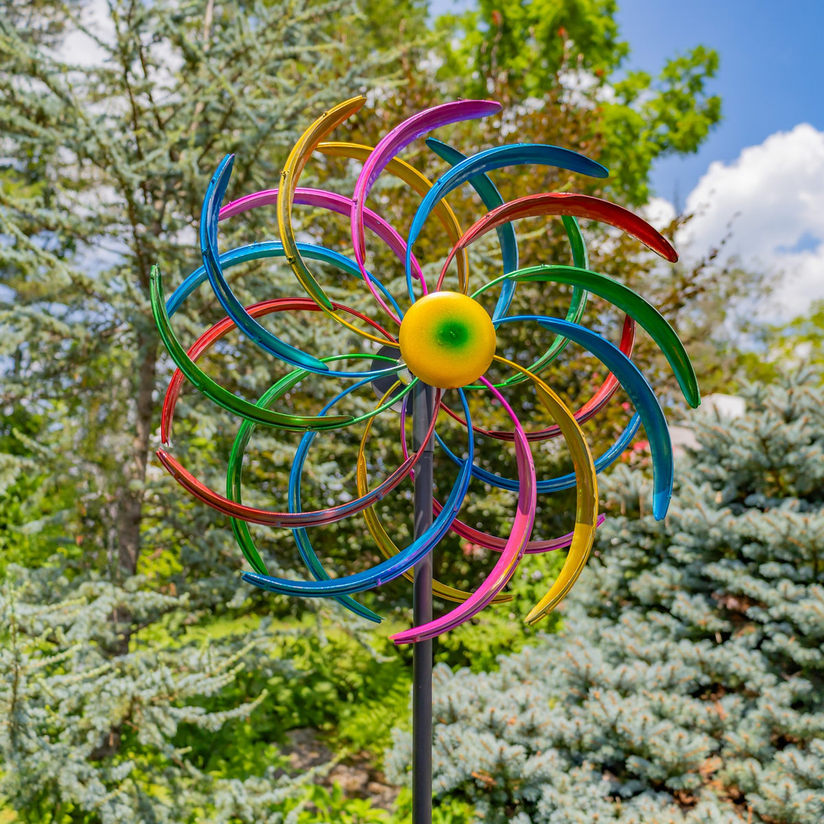 Bright jewel-tone windmill spinner on its stake among garden trees