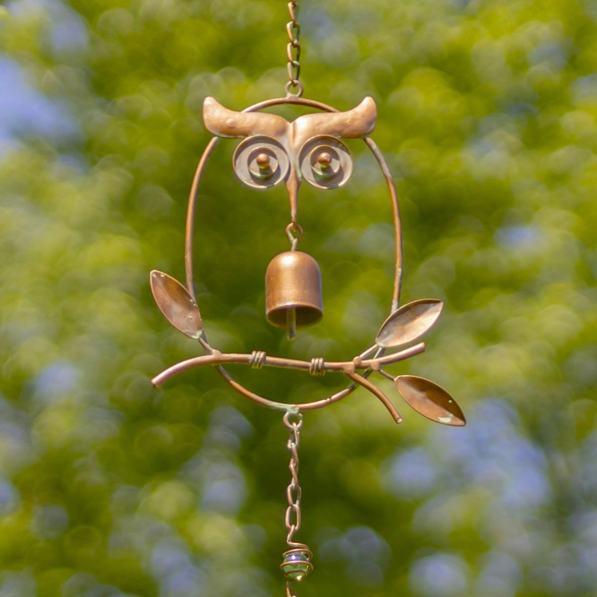 Close-up of an owl-shaped rain chain link with a small bell and metal leaves.