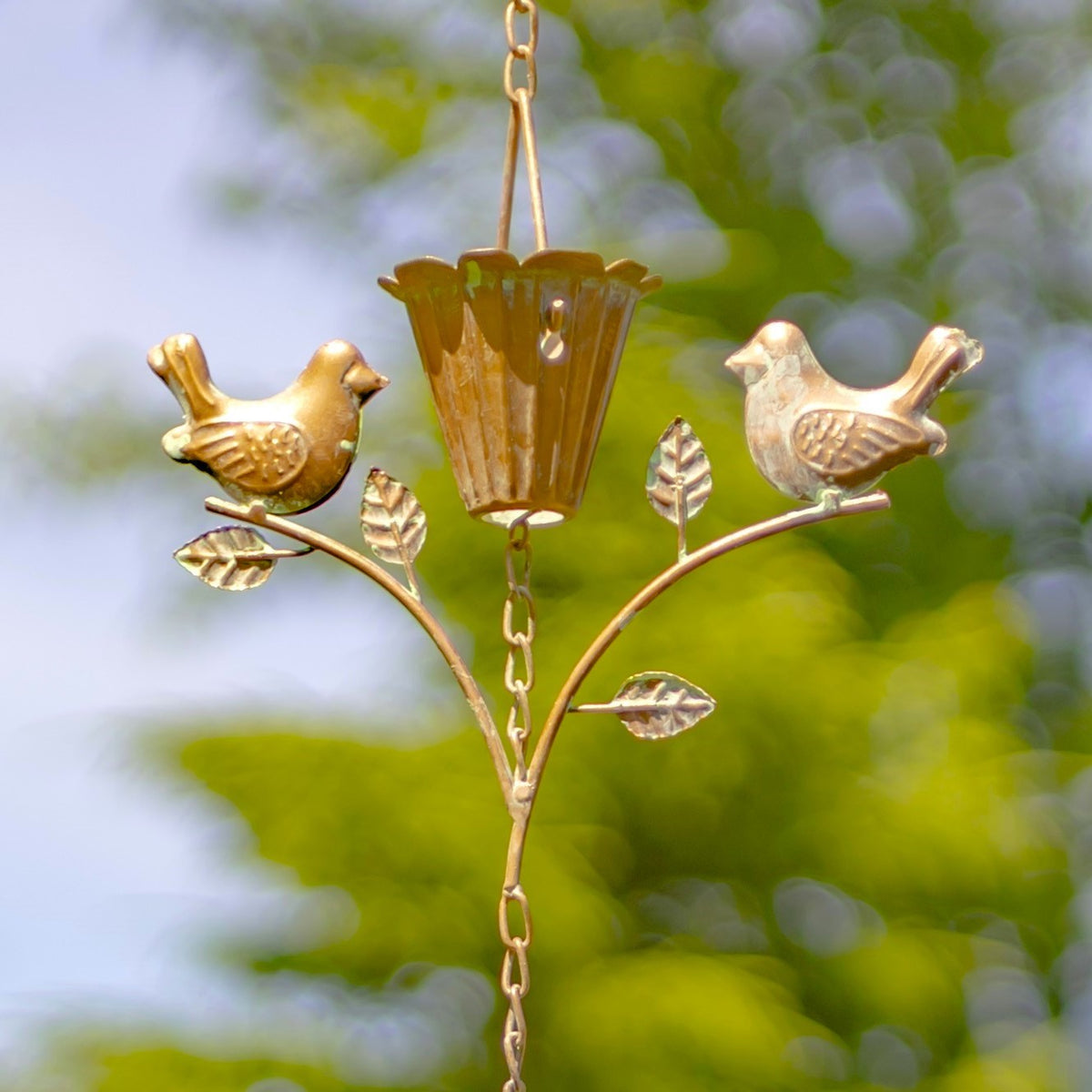 Close-up of two birds perched on curved branches beside a fluted cup and metal leaves.