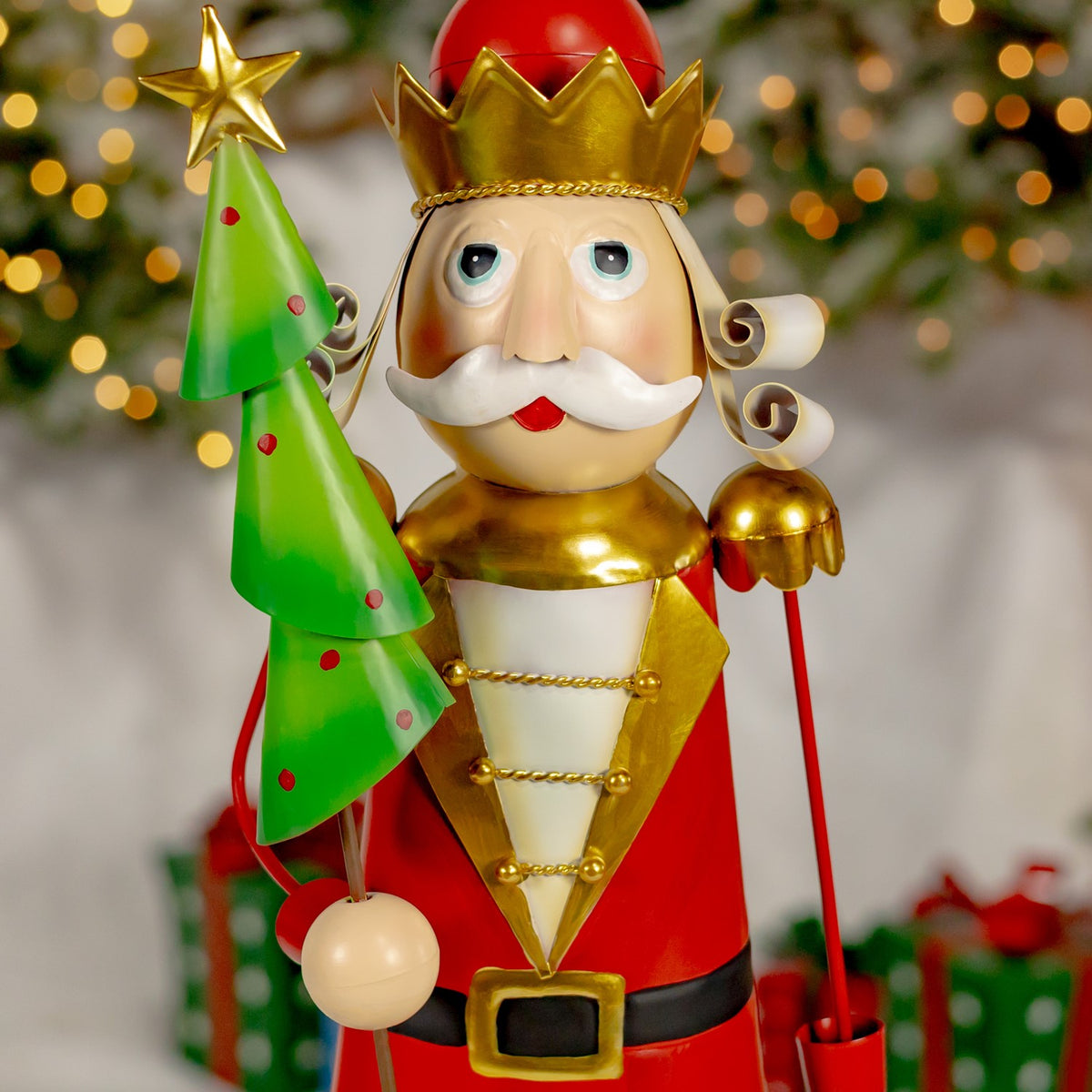 A red-coated nutcracker holds a green tiered tree, with gold shoulder pieces and a crown.