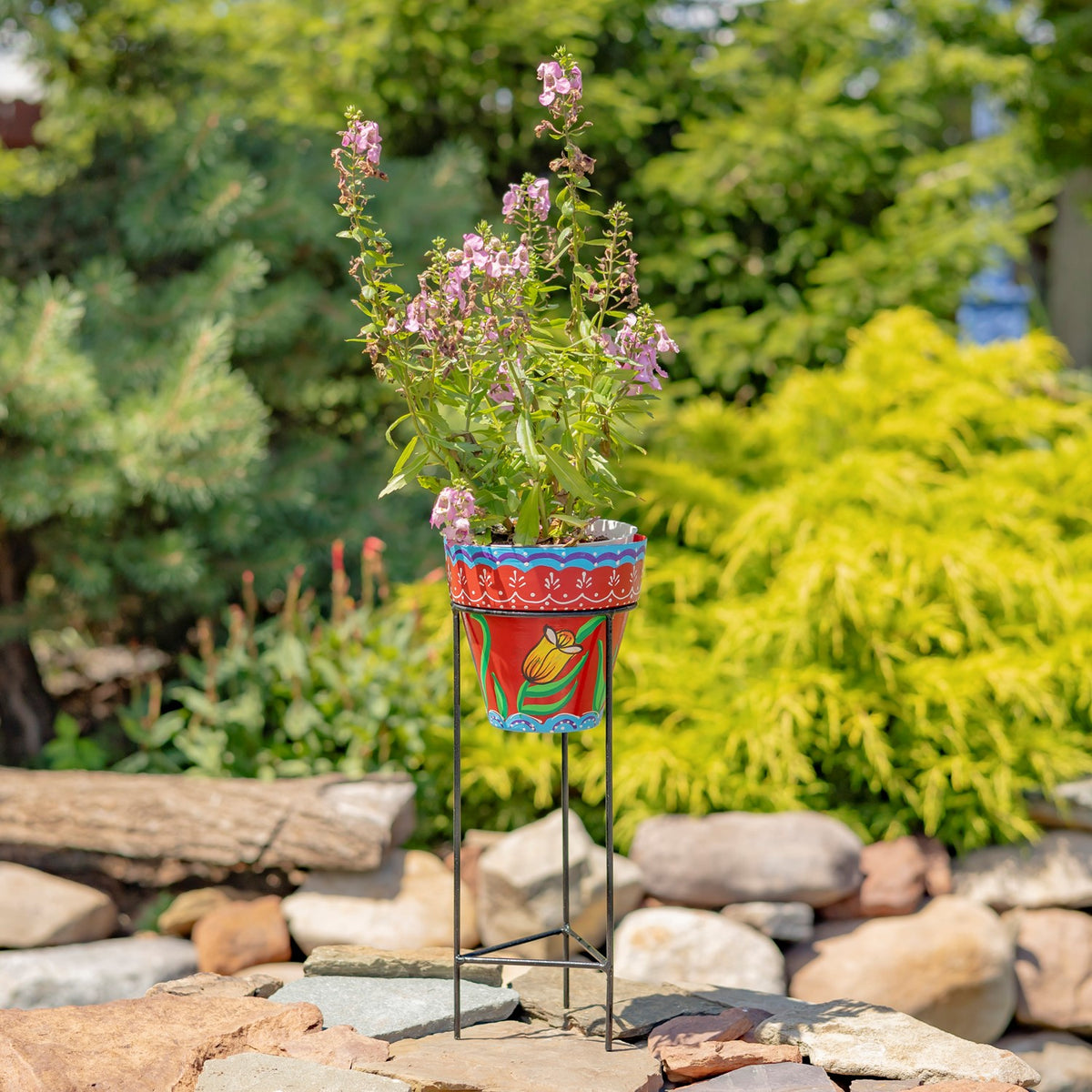 Red flowerpot with a blue patterned rim and yellow flower motif, raised on an iron stand.