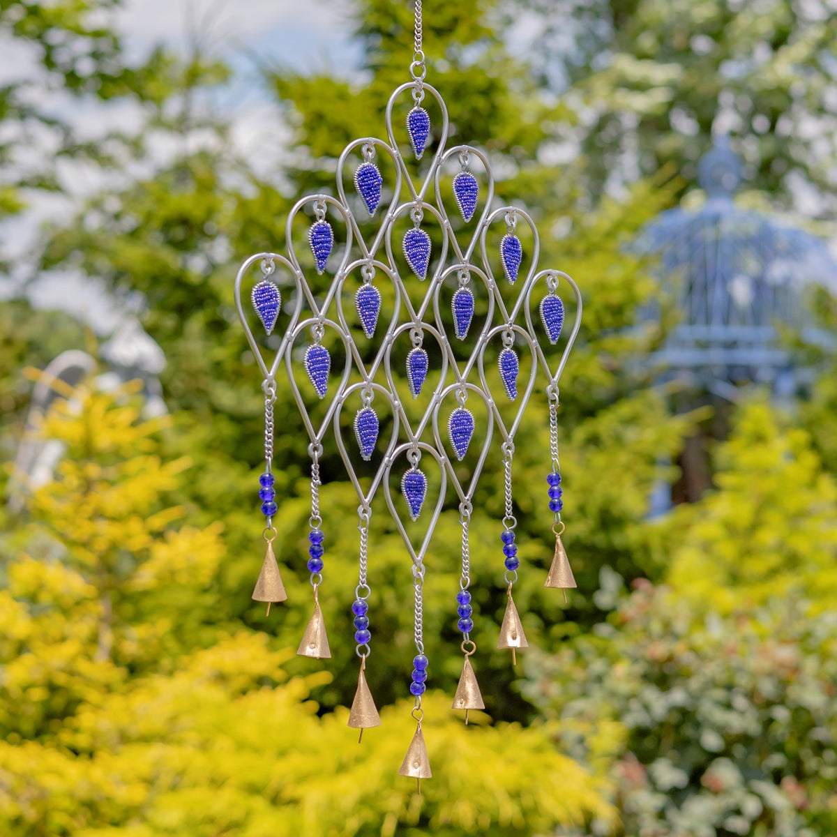Silver-tone wind chime with deep blue accents and dangling bell-shaped pieces against a leafy garden.