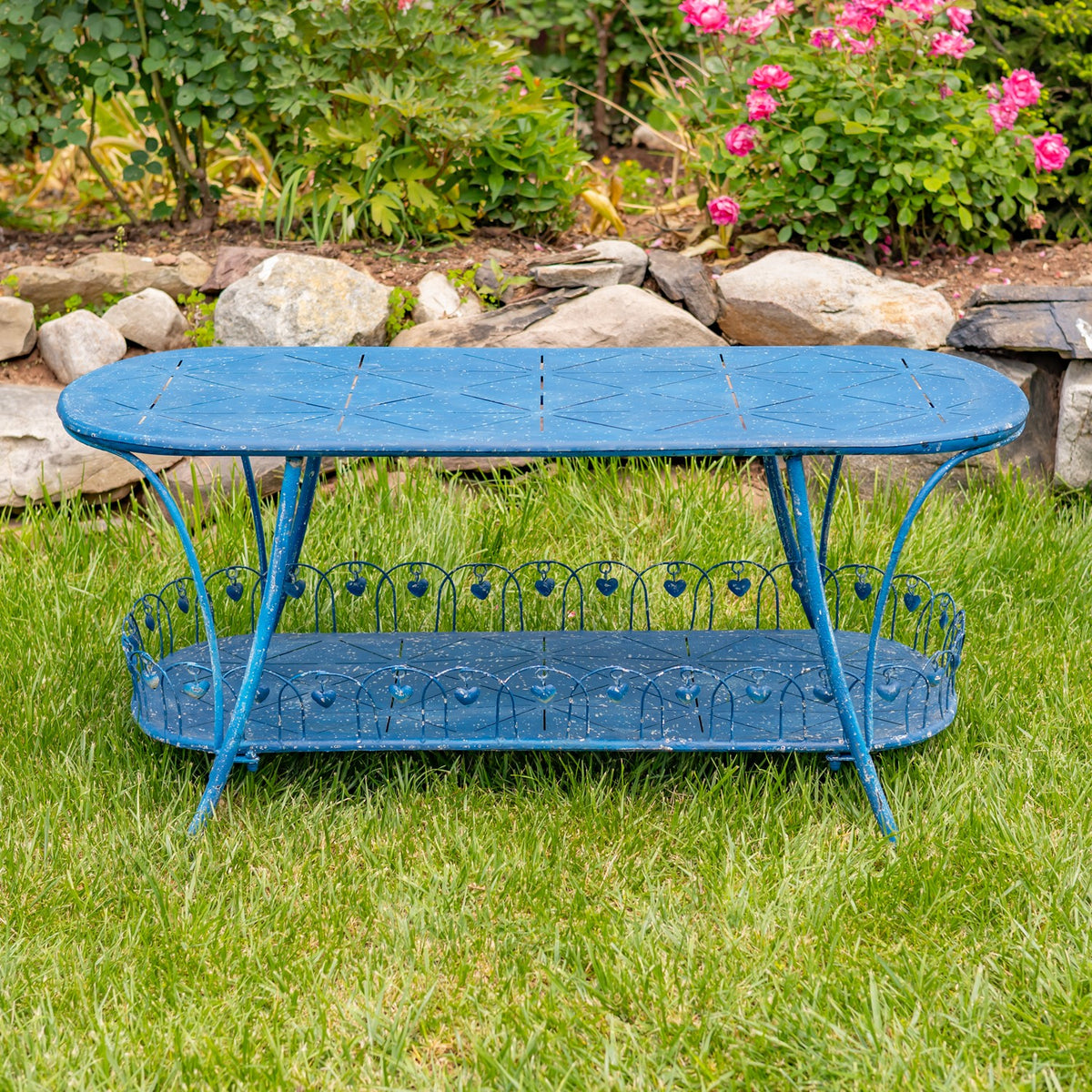 Blue oval iron garden table with a patterned lower shelf, photographed on grass.