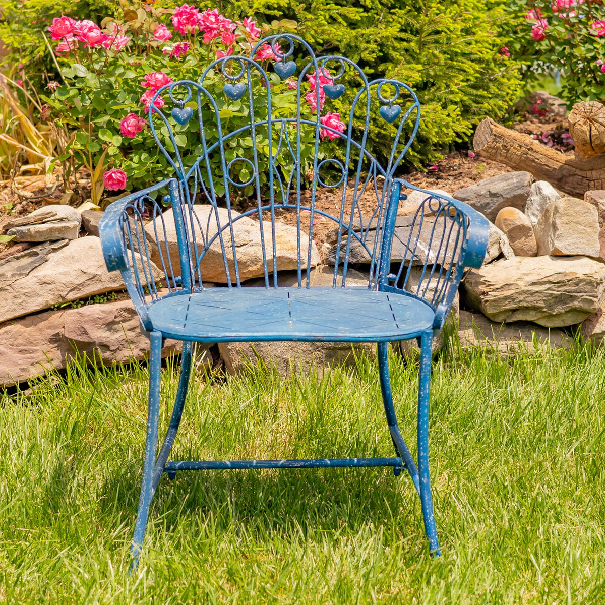 Blue metal garden armchair on grass, with heart-shaped details among flowers and rocks.