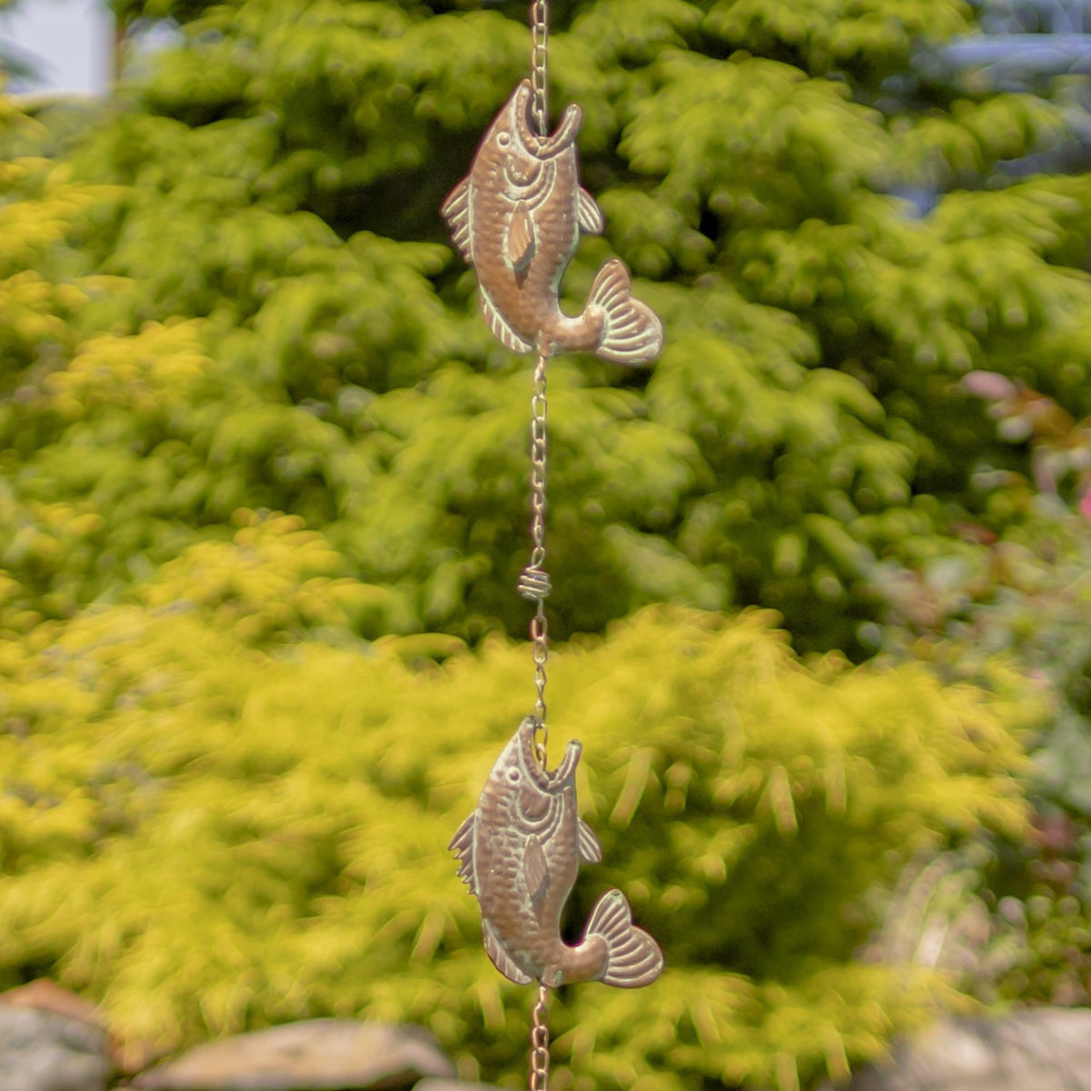 Two sculpted fish ornaments link the chain, shown against softly blurred garden foliage.