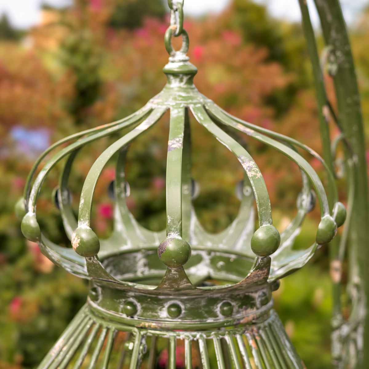 Close-up of a green metal chair crown with curved bars and a hanging chain.