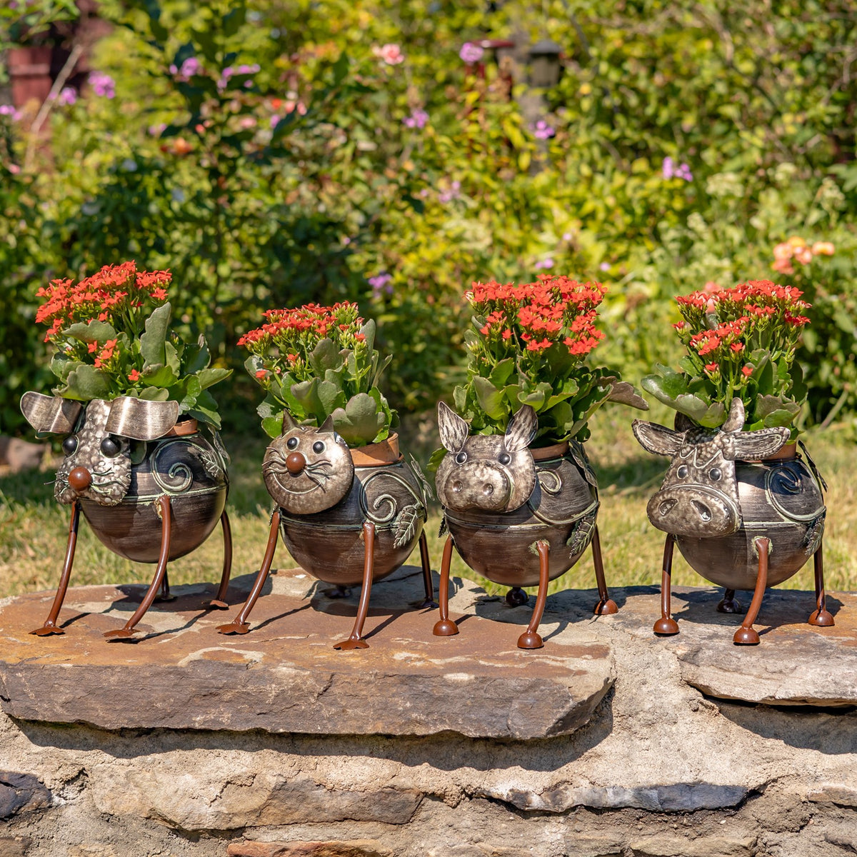 Four different animal-shaped metal planters, each filled with red flowers, sit together outdoors.