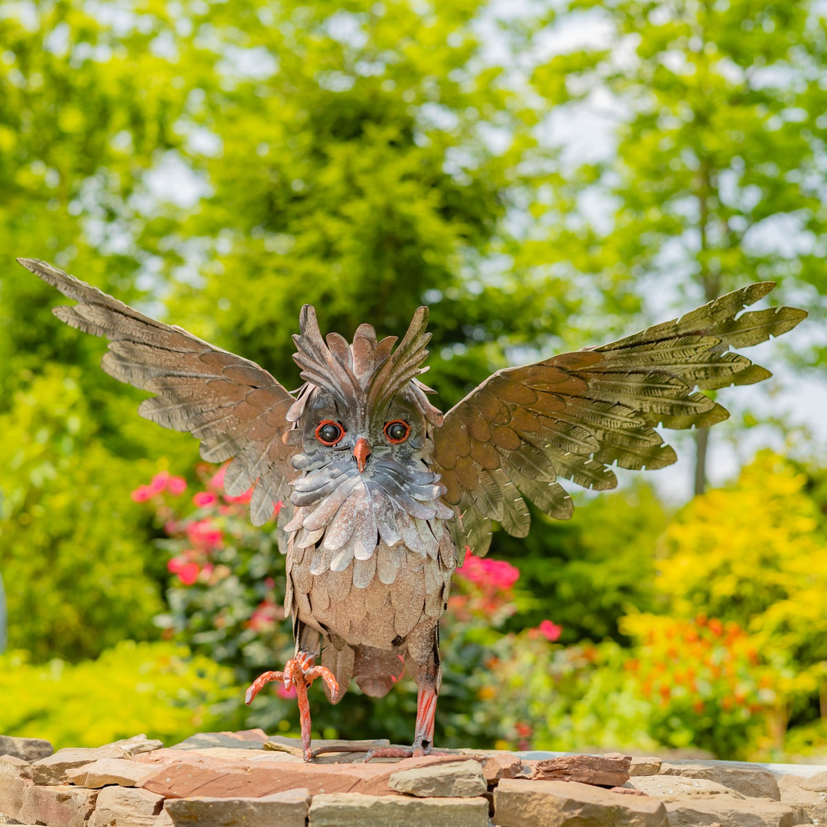 Owl sculpture faces forward with both wings spread above a stone ledge.