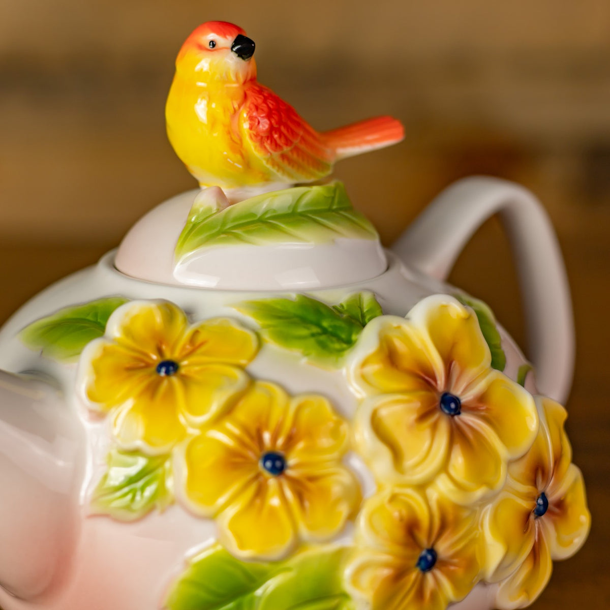 Close view of the bird-shaped lid finial and raised yellow flowers on the teapot.