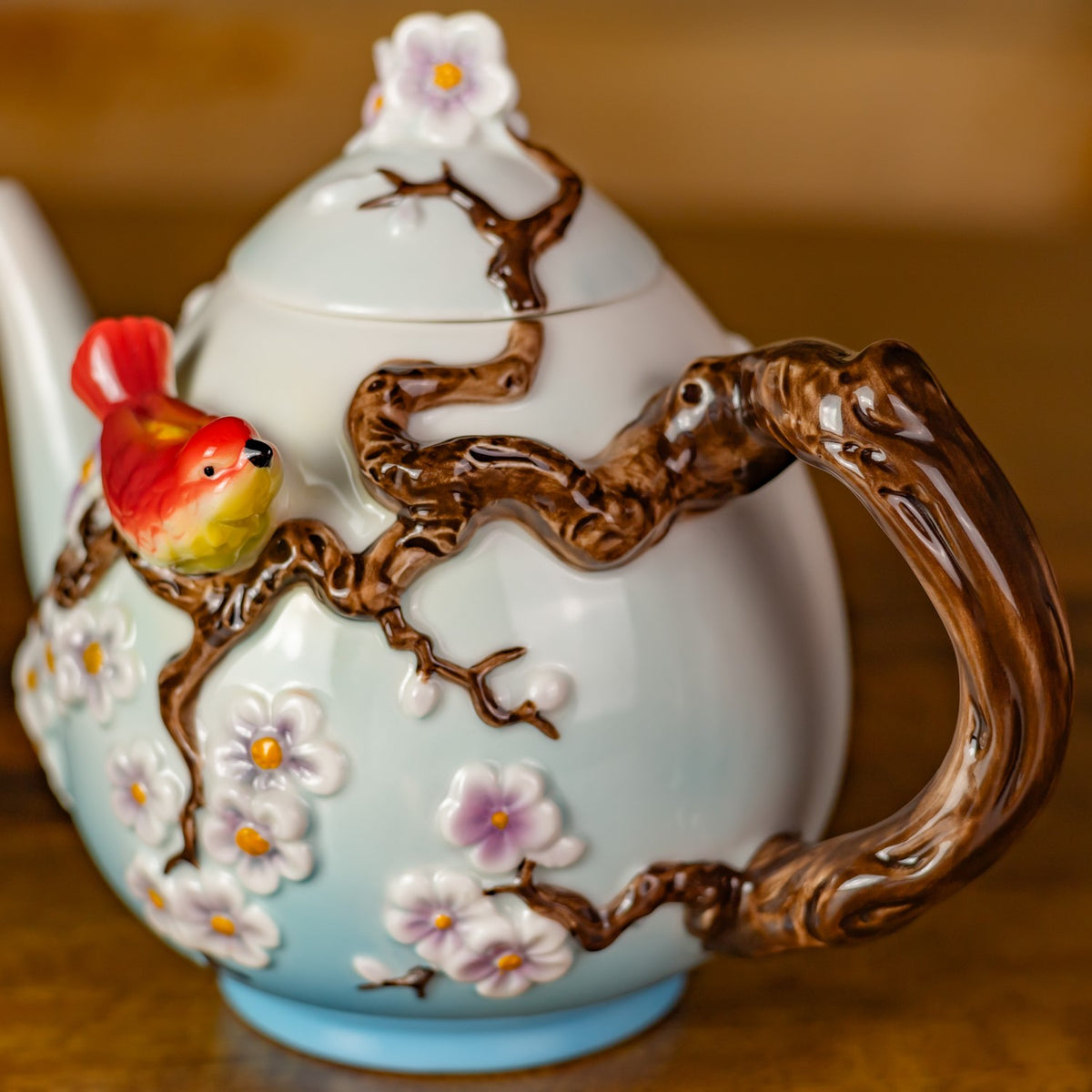 Close-up of the teapot’s sculpted brown branch handle and floral decorations, with part of a red bird visible.