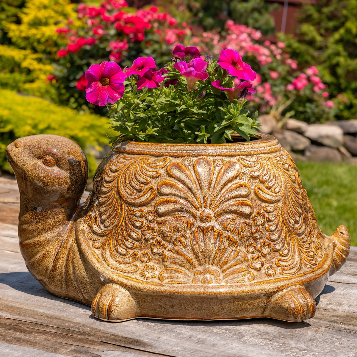 Turtle planter facing forward, with pink flowers above its raised floral shell pattern.