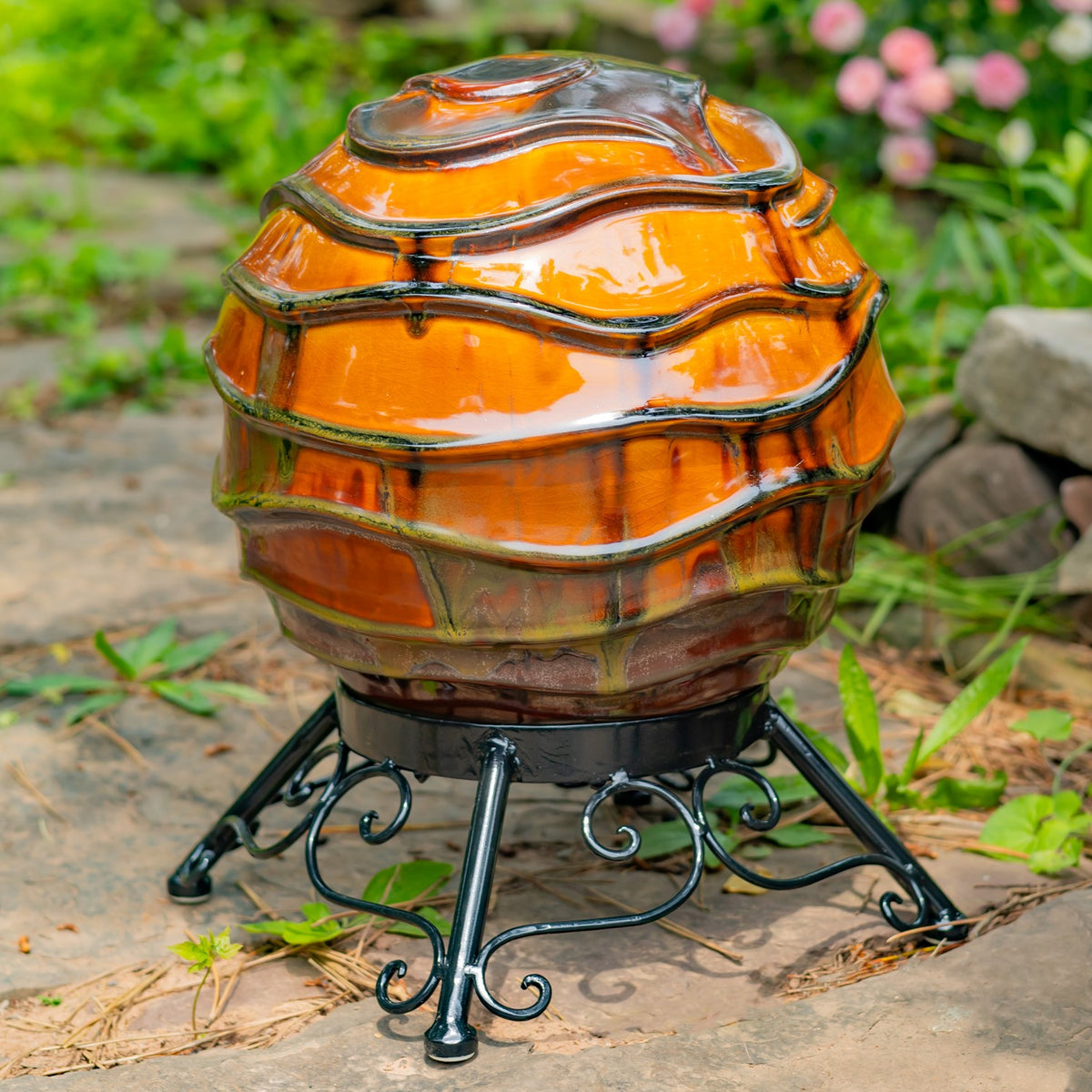 A large orange and gray rippled globe sits on a curled black metal stand on a garden path.