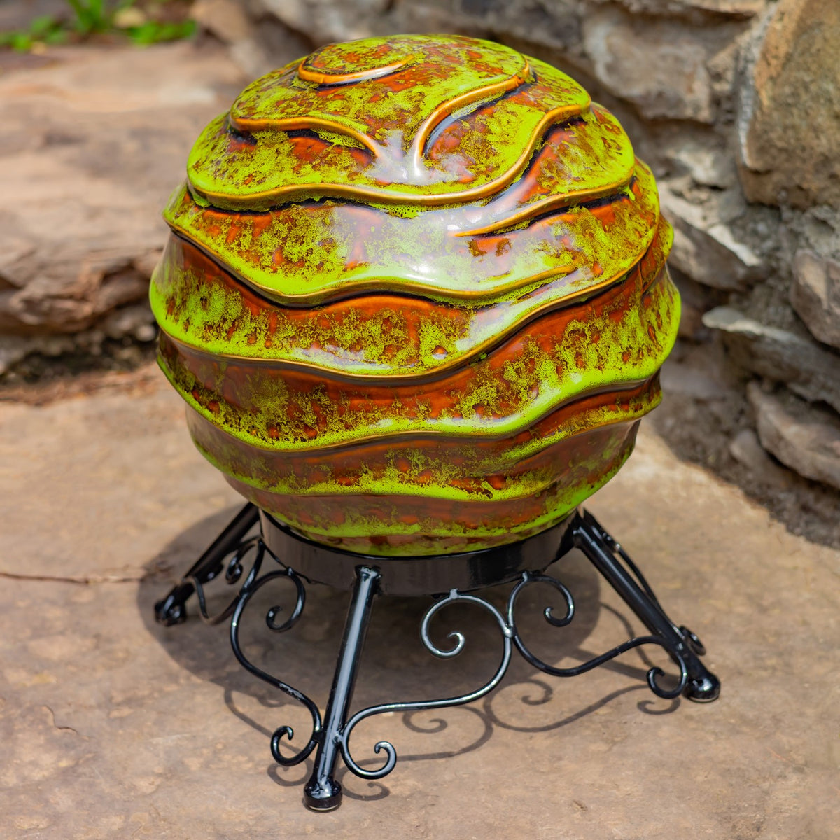 A glossy green and gold globe with raised wavy bands sits on an ornate black metal stand.