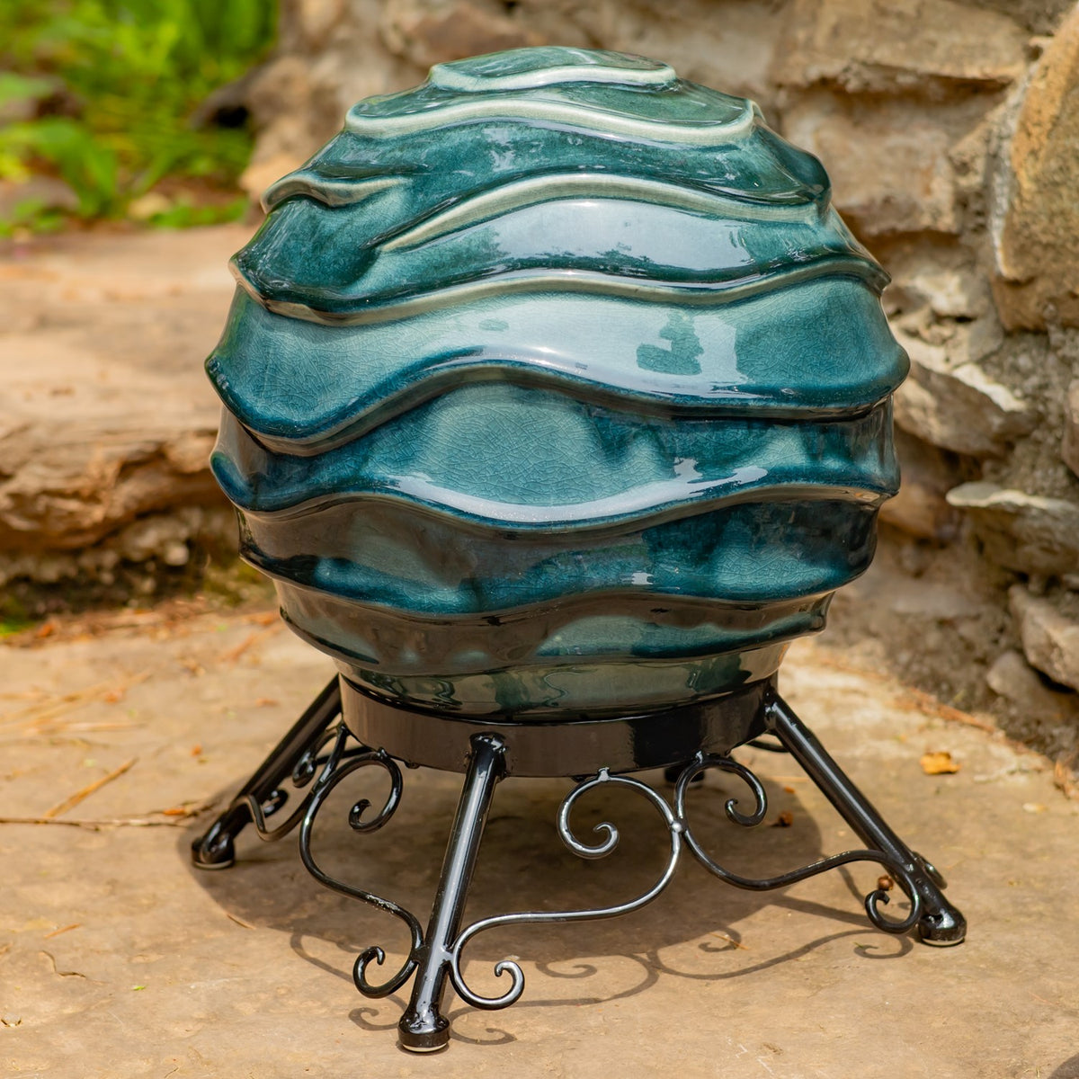 A large glossy teal globe with raised wavy bands sits on an ornate black metal stand.