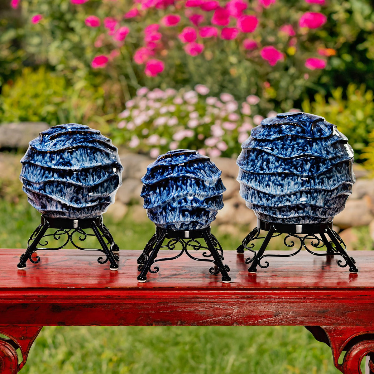 Three differently sized blue-and-white globes on ornate black stands arranged on a red table.