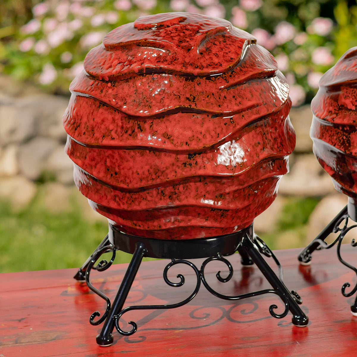 Close view of a large speckled red globe with layered ridges on an ornate black metal stand.
