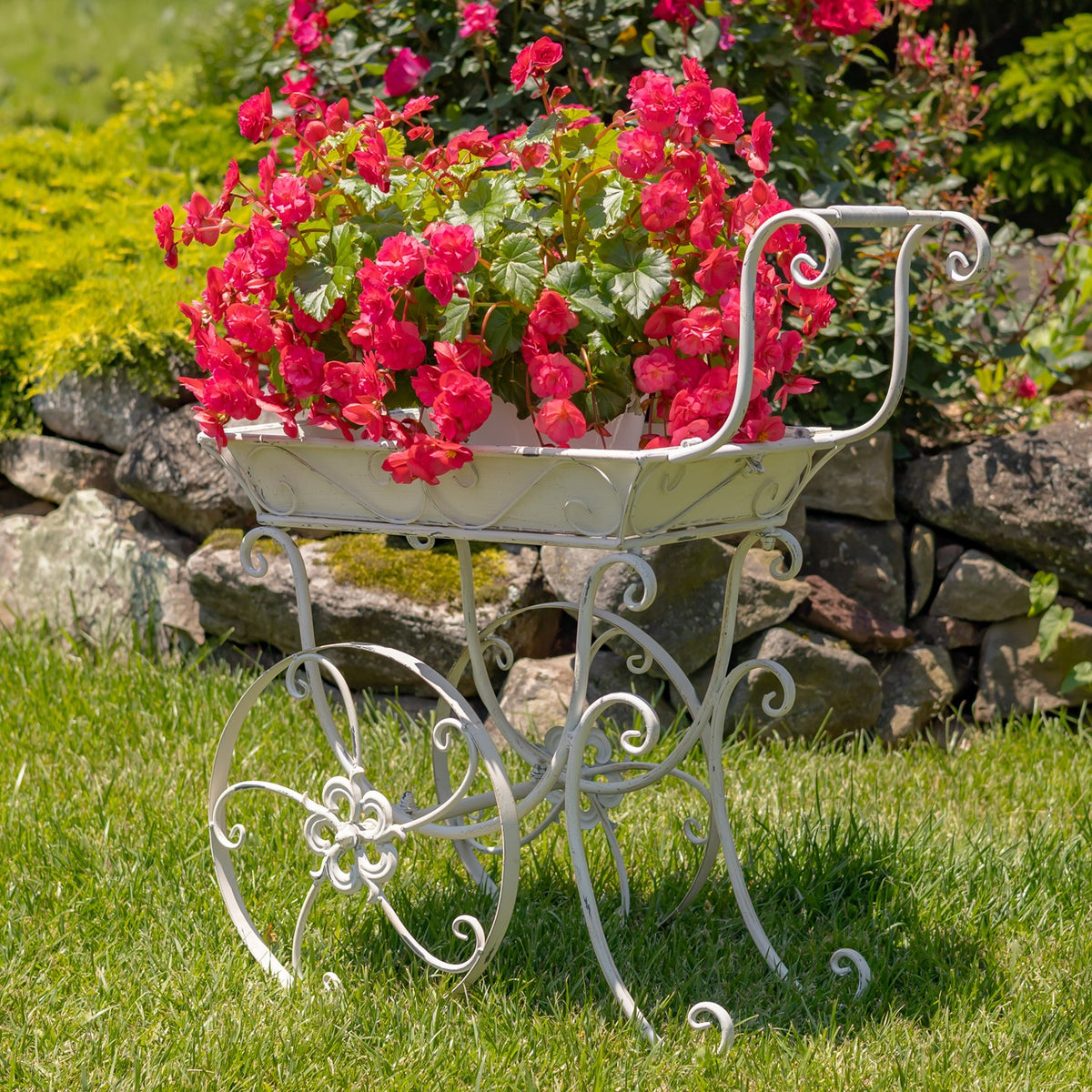 Ornate white garden cart with pink flowers, showing its curled handle and decorative wheel frame.