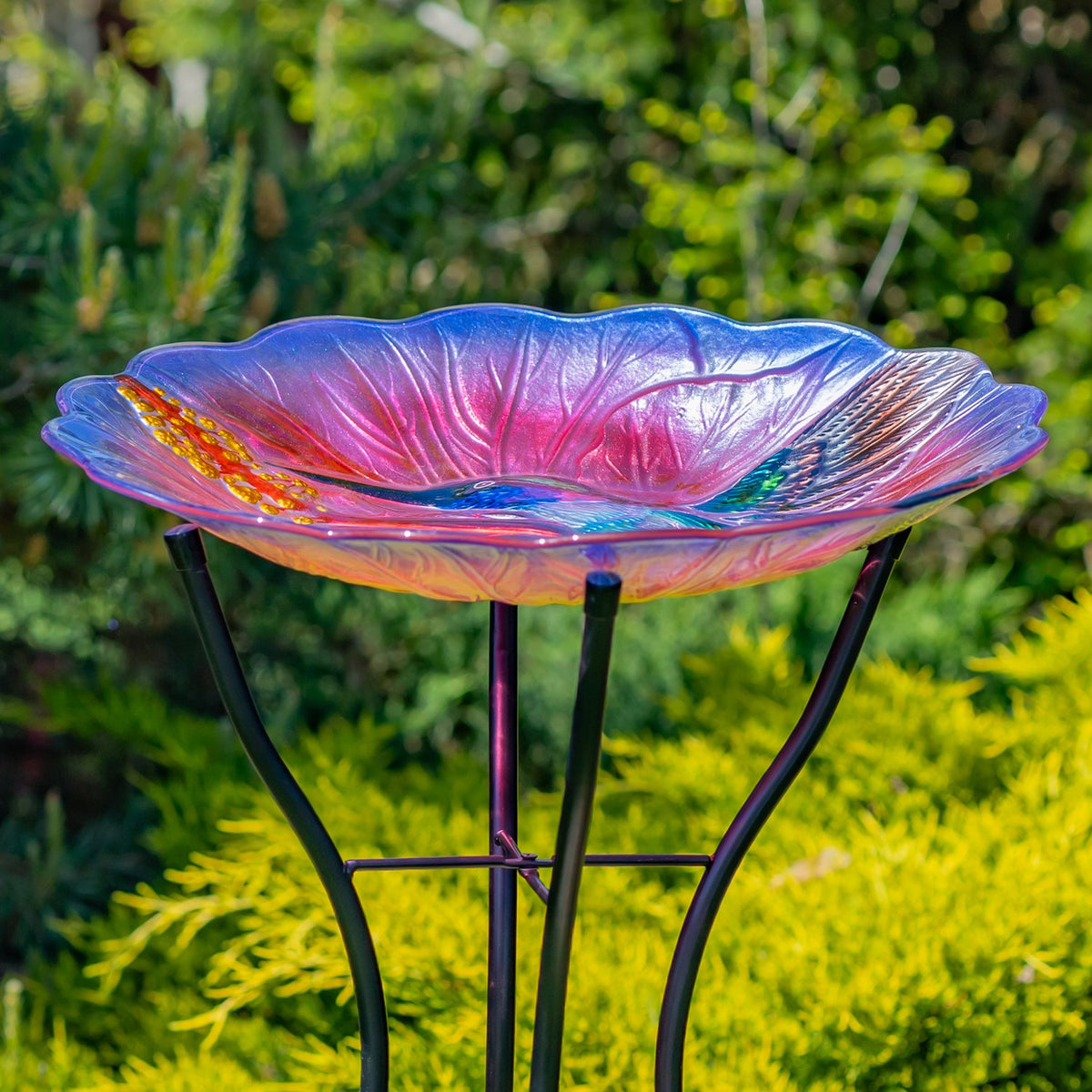 Side view of the shallow, flower-shaped glass bowl resting on a black metal stand in a garden.
