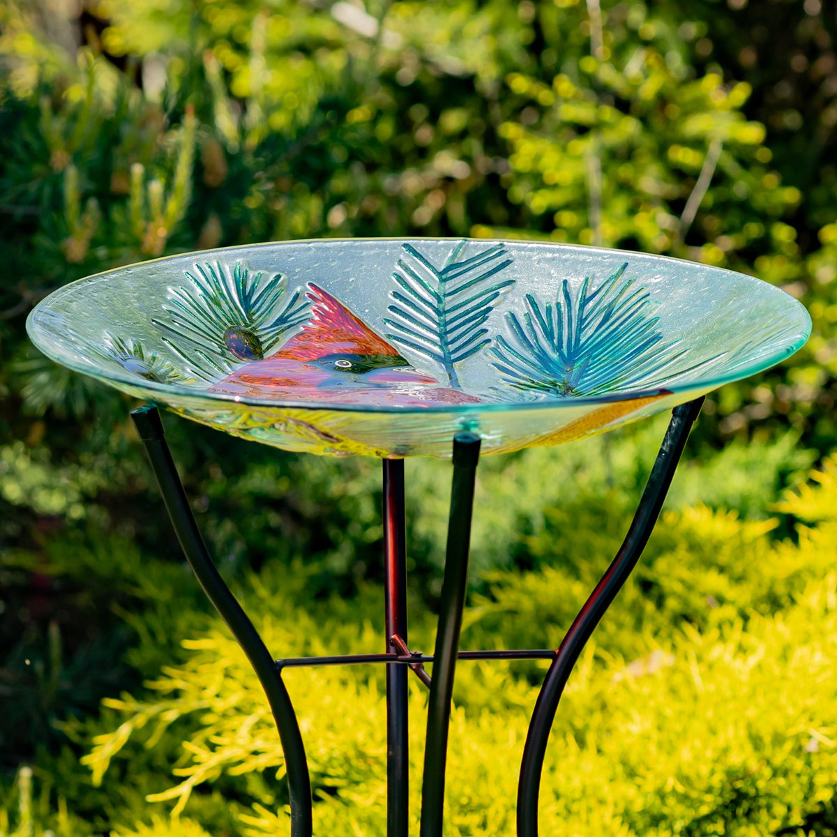 Shallow cardinal glass bowl resting on a black iron stand among greenery