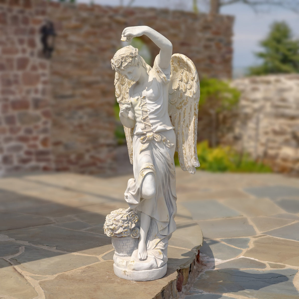 Full view of the winged angel statue standing on a sculpted base in a stone-paved courtyard.
