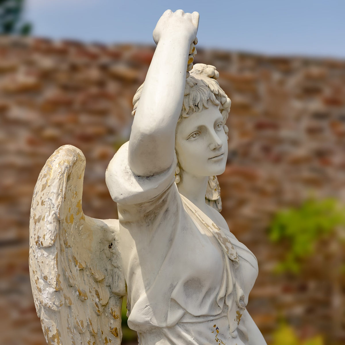 Close-up of the angel’s face, raised arm, draped bodice and weathered wing.