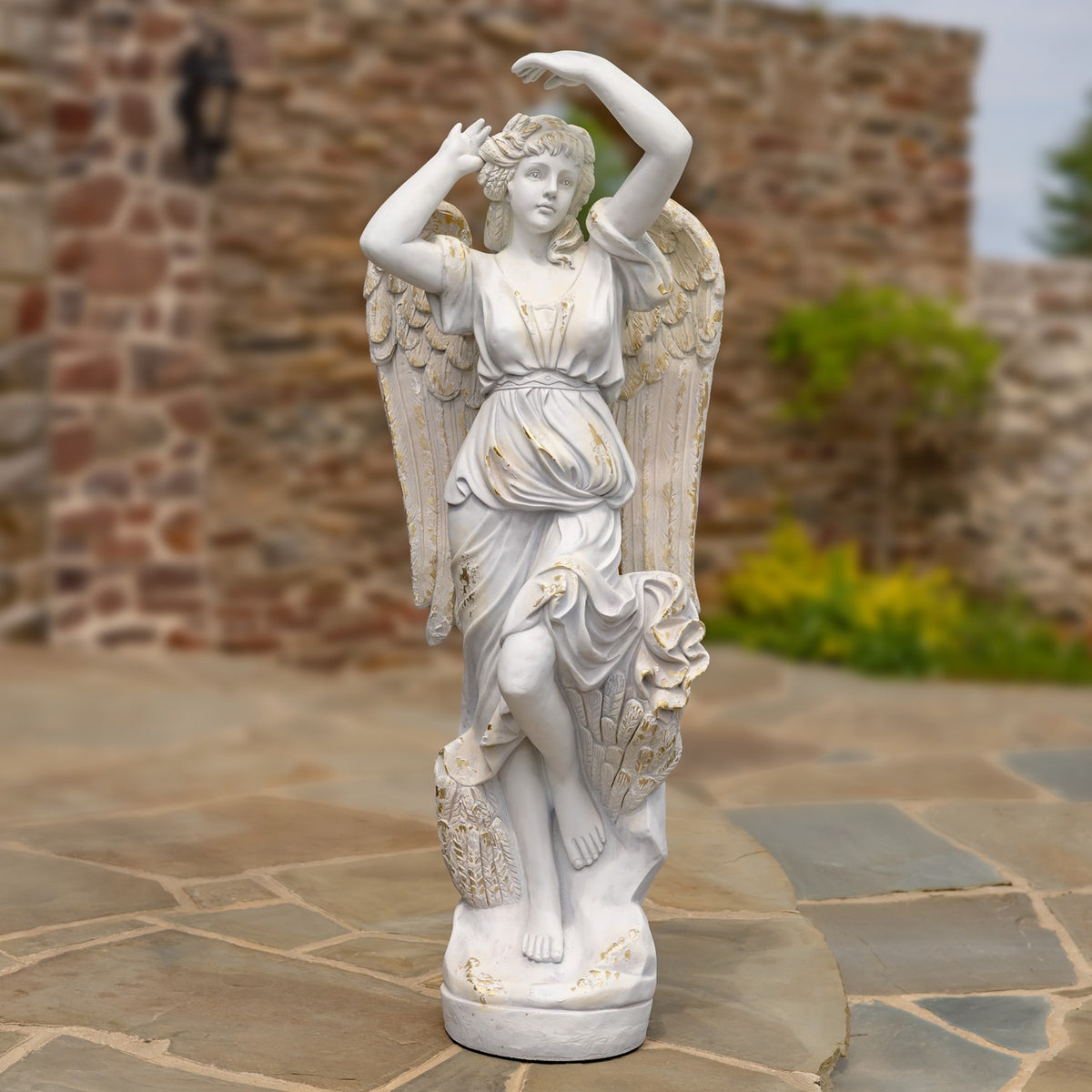 Full-length angel statue stands on a round base with one knee raised and arms lifted overhead.