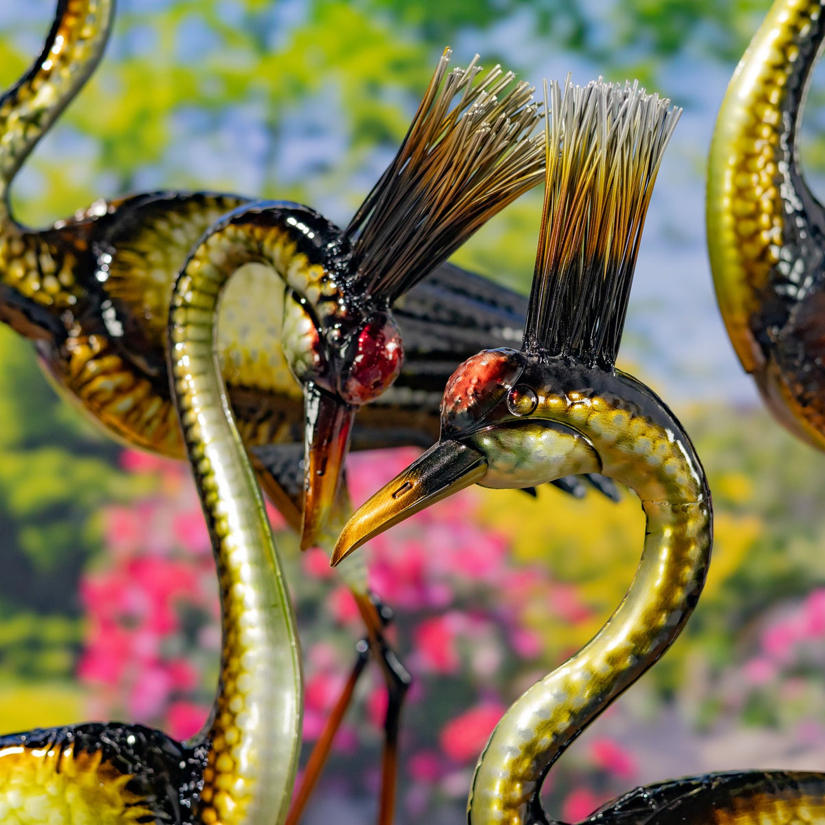 Two metallic heron figurines face each other, showing their curved necks and textured gold-and-black finish.