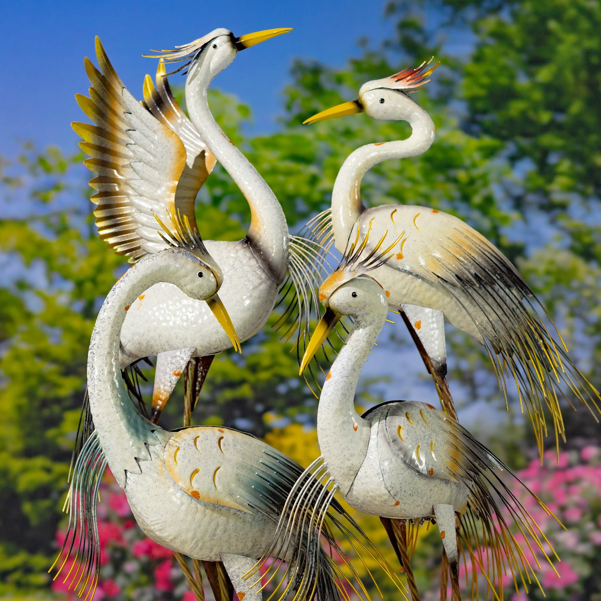Four sculpted herons stand together outdoors, their pale bodies accented with gold and dark feather details.