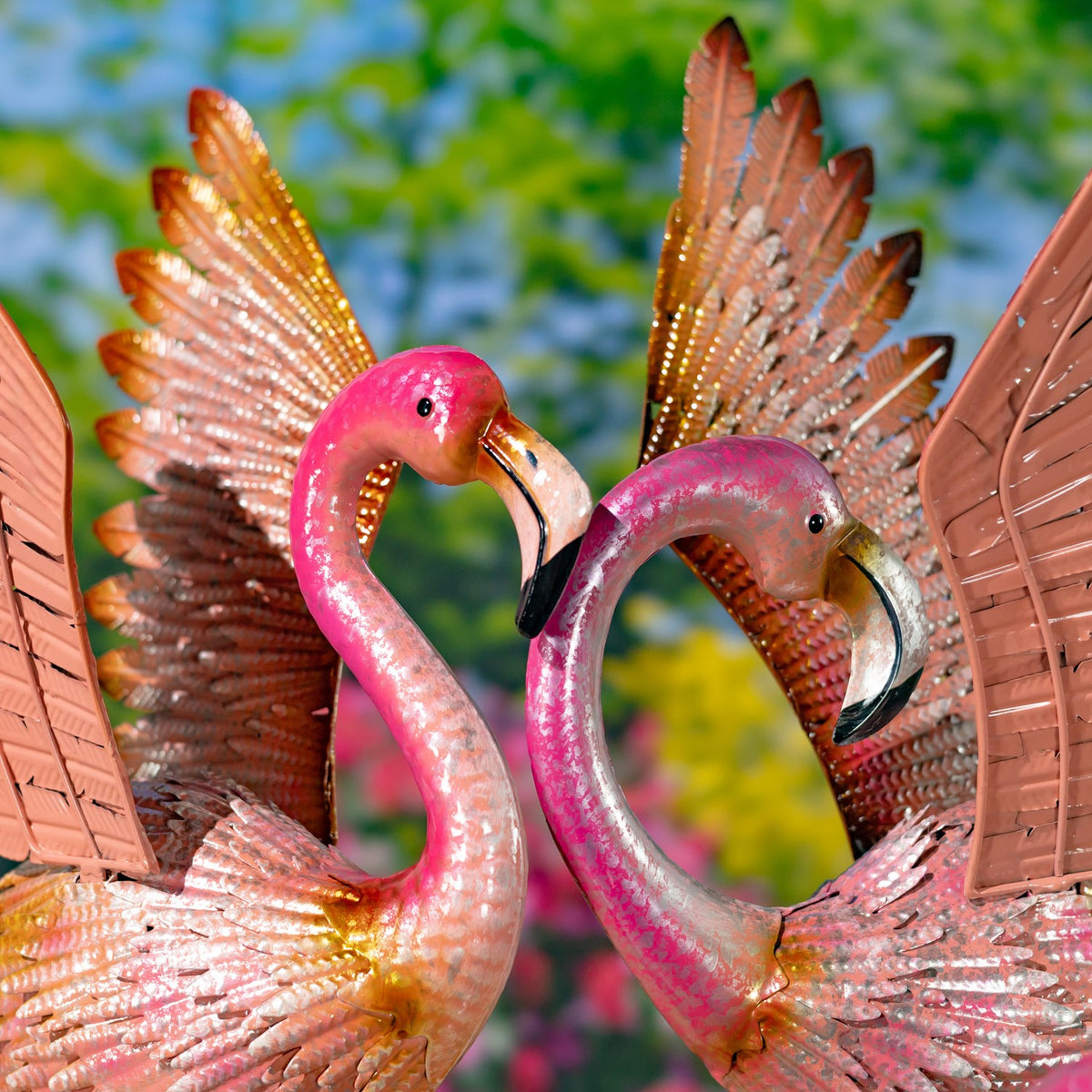 Two pink flamingos with raised wings stand side by side against a leafy garden backdrop.