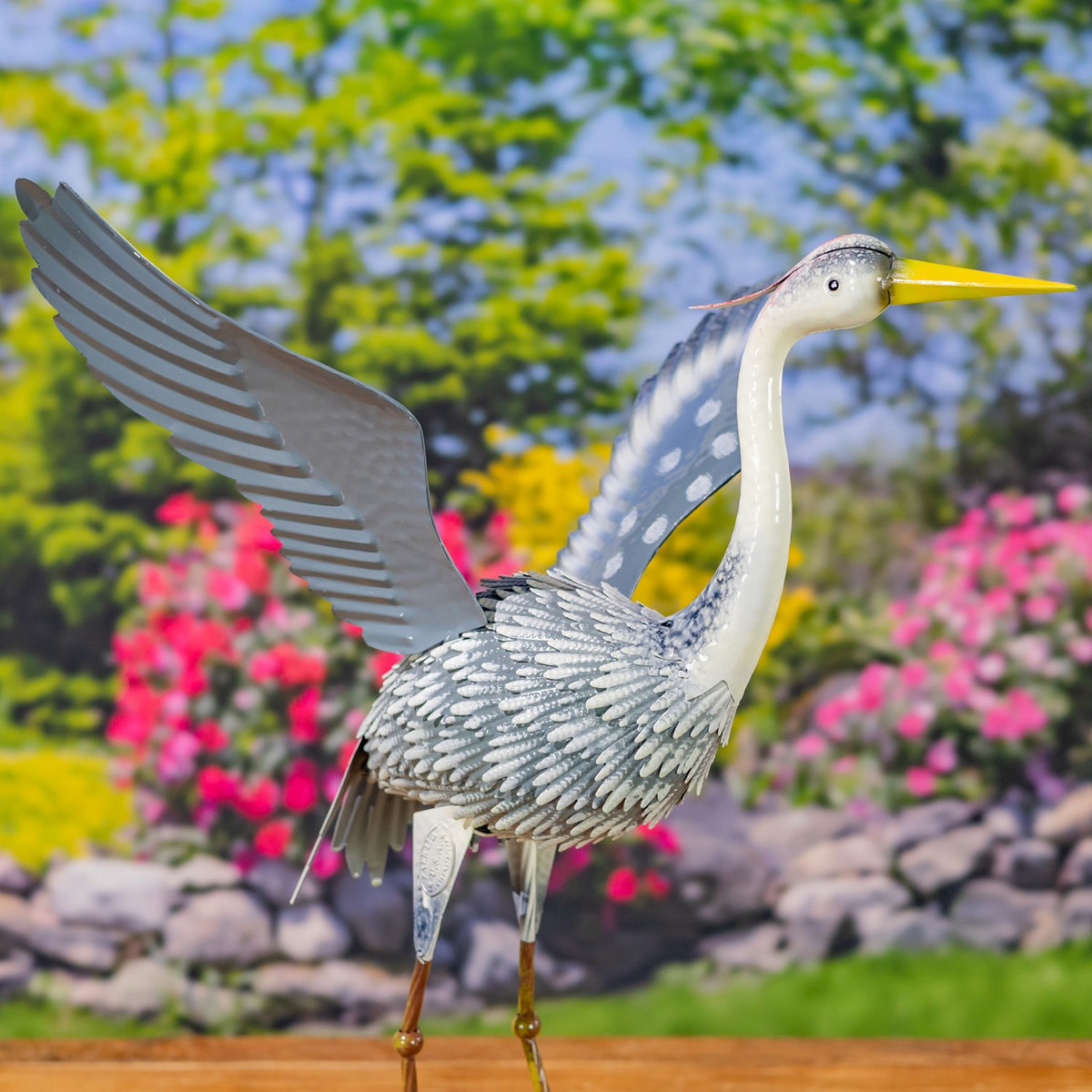 A metal heron figure stands with its neck extended and one broad wing raised.