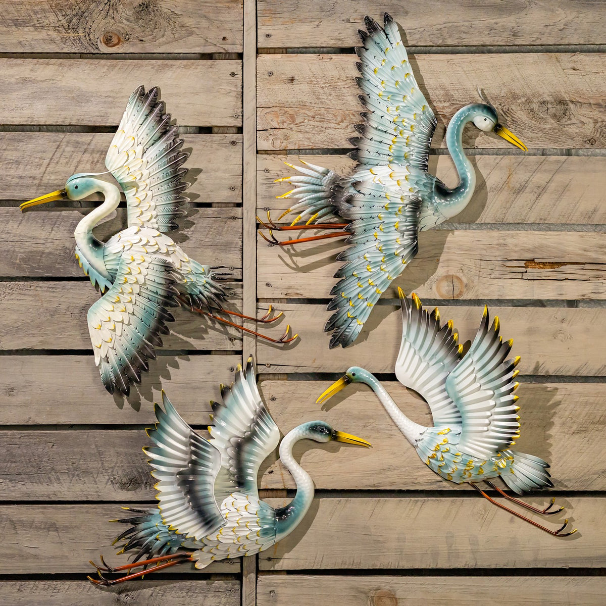 Four colorful crane wall decorations arranged in different flying poses on a weathered wooden wall.