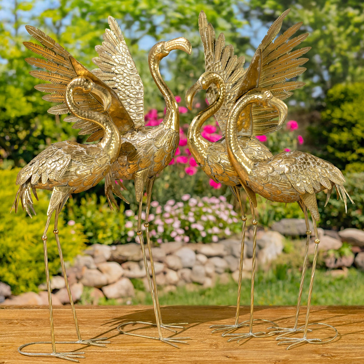 Four gold flamingo figurines stand together on a wooden surface, showing varied poses and raised wings.