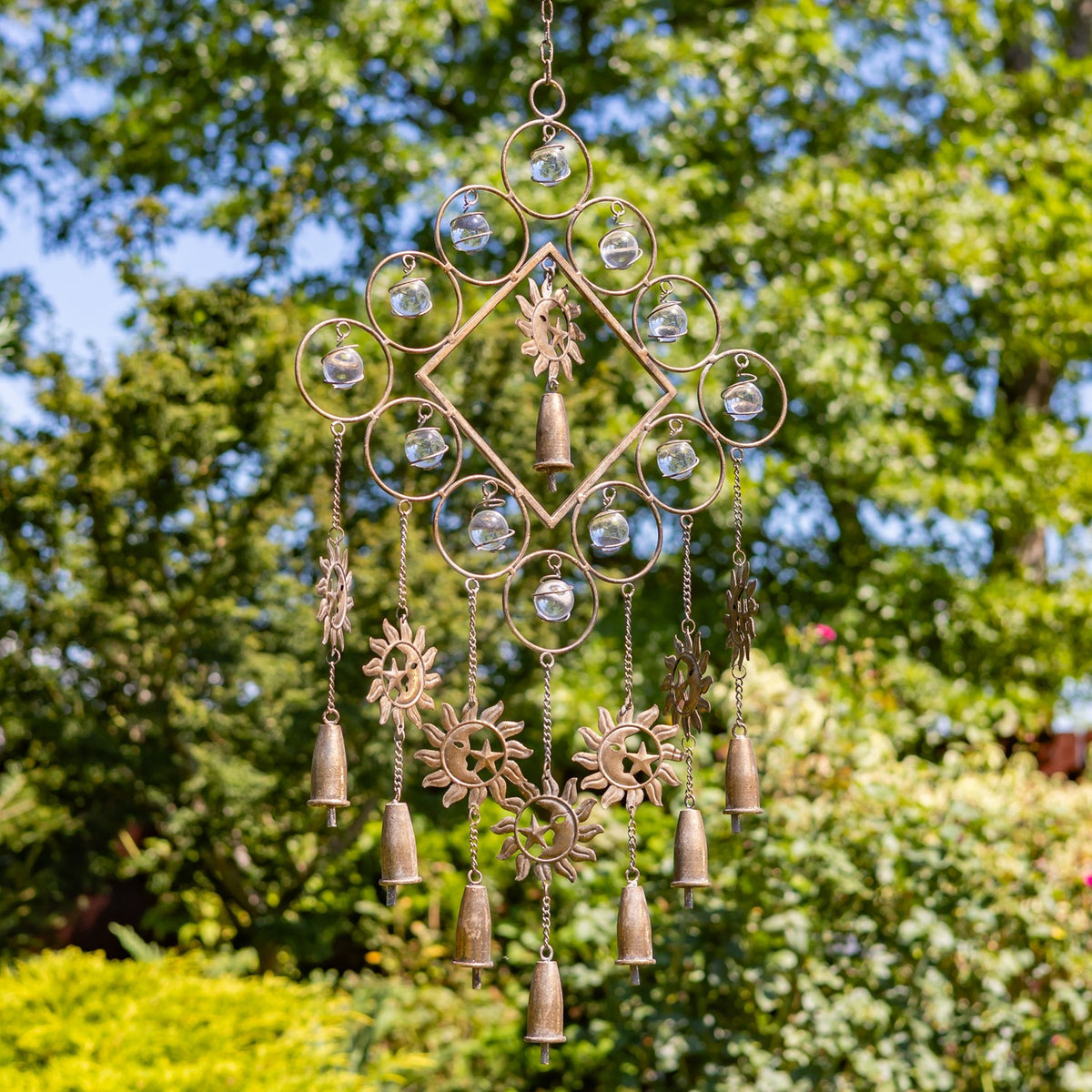 Hanging metal chime with a ringed geometric frame, small reflective accents, sun-shaped ornaments, and dangling bells.