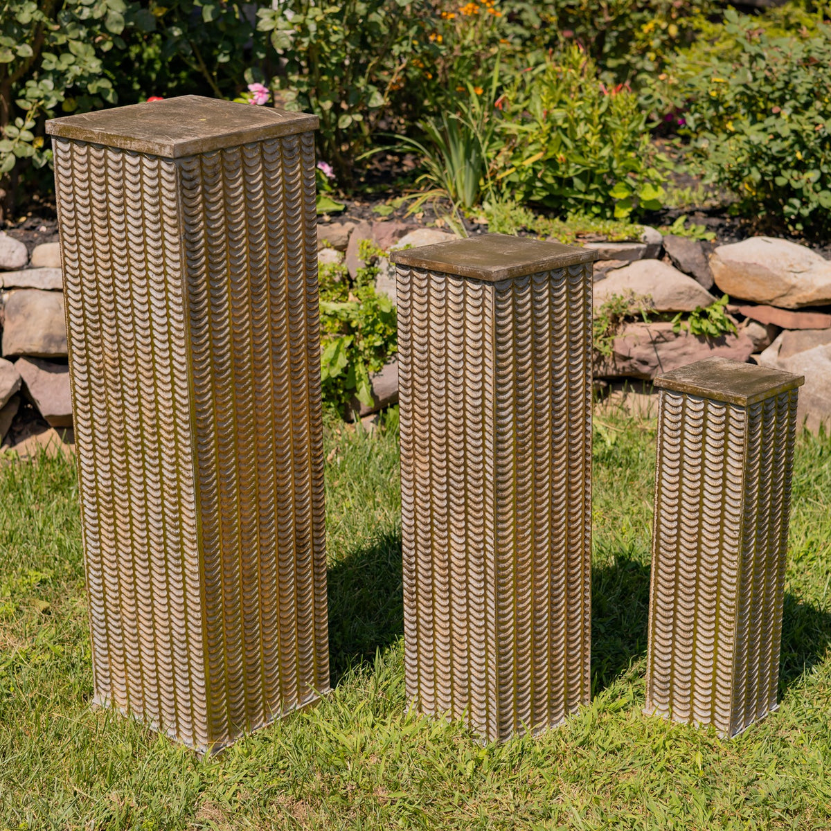 Three gold-toned pillars of graduated heights shown together without flowers in a garden.