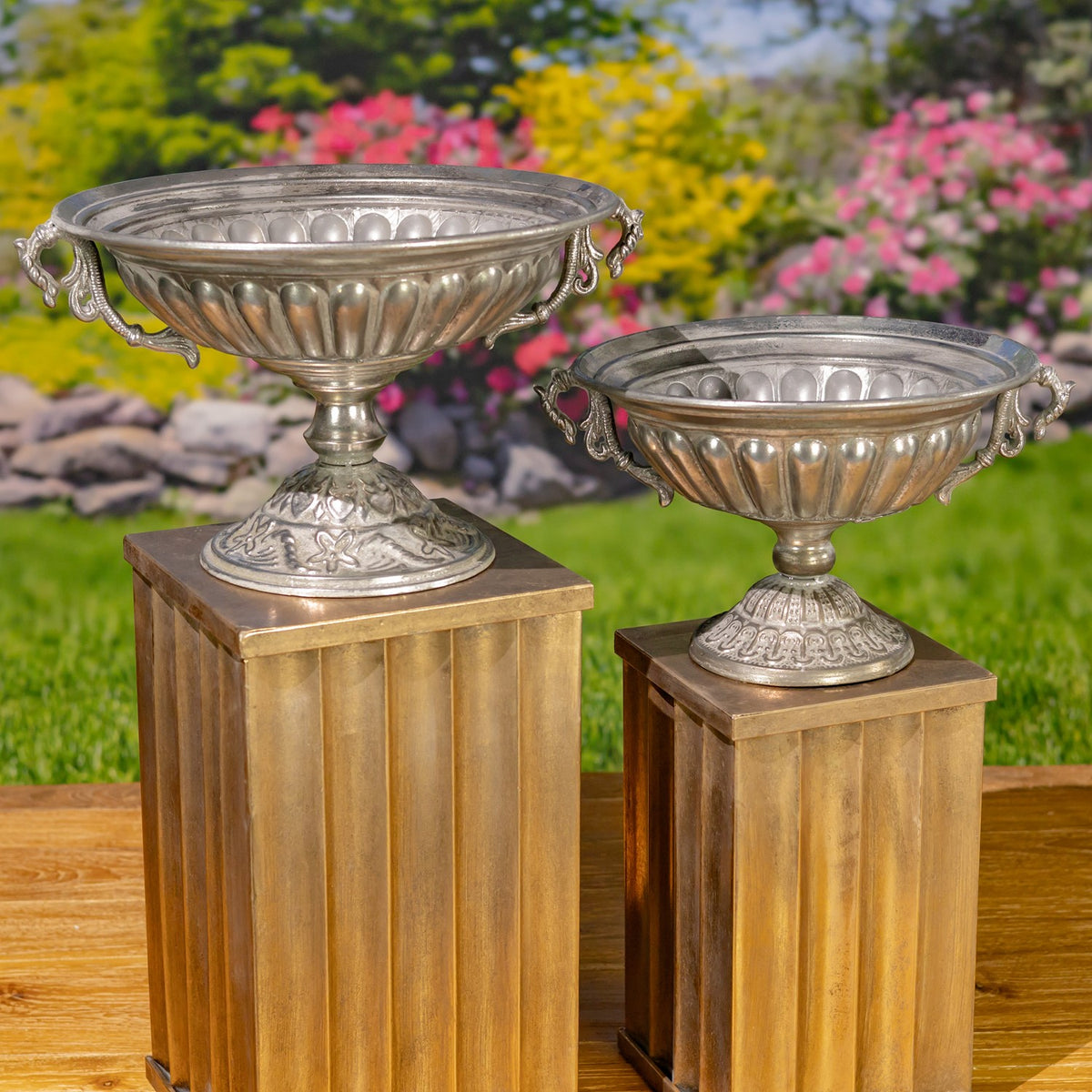 Two silver urns of different sizes are displayed on separate wooden stands.