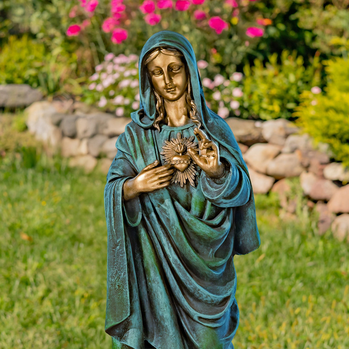 Mary holds a radiant heart at her chest, with one hand raised, against a flower-filled garden.