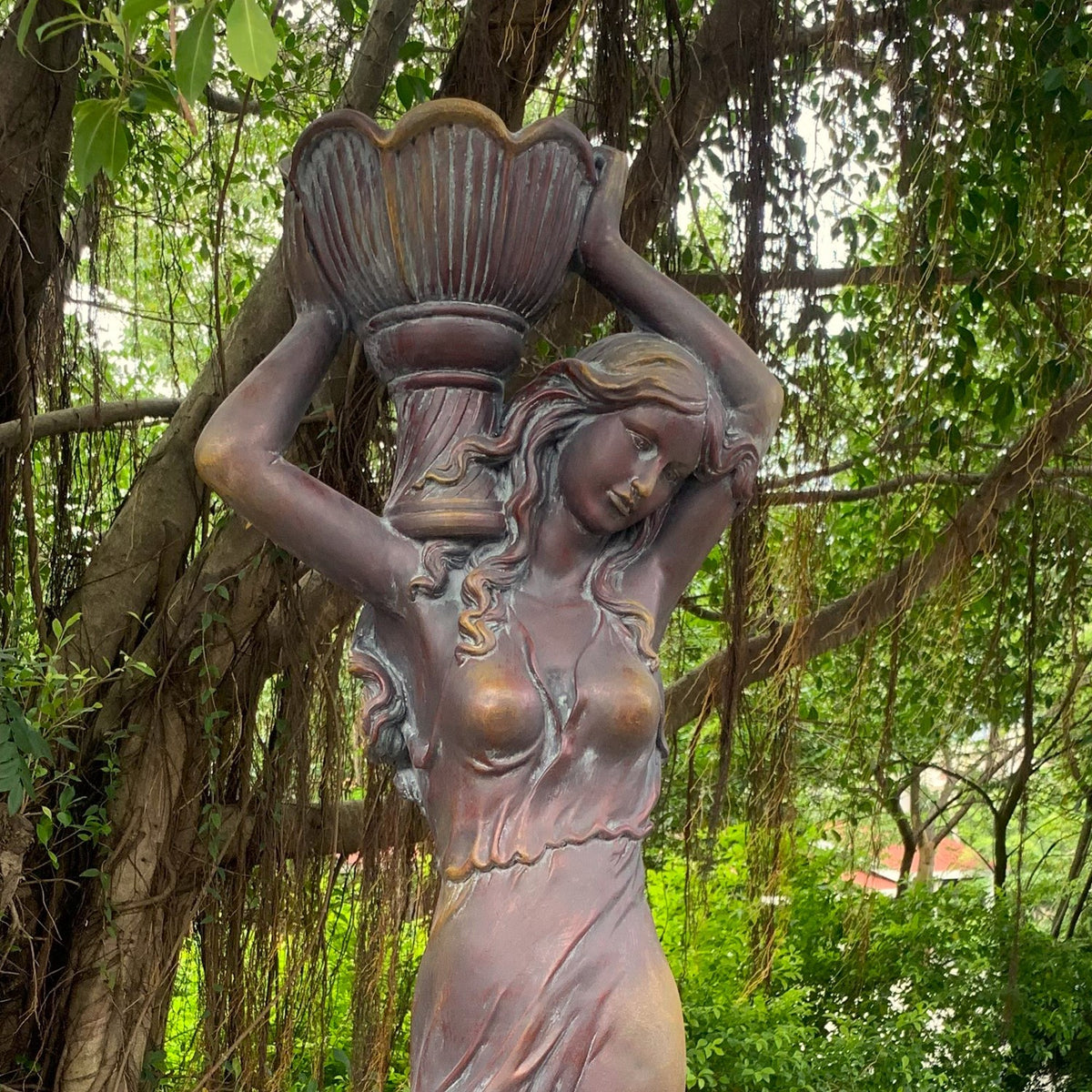 Closer front view of the statue shows the woman's face, flowing hair, dress, and raised flower pot.