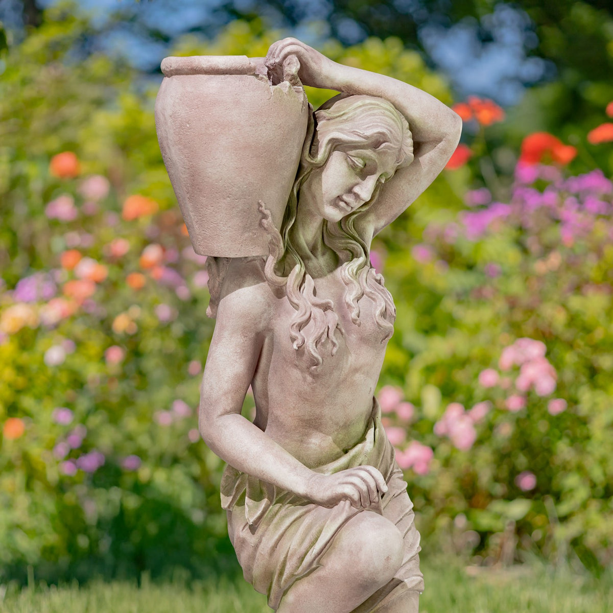 Close view of a kneeling woman statue holding an urn over her shoulder in a flower garden.