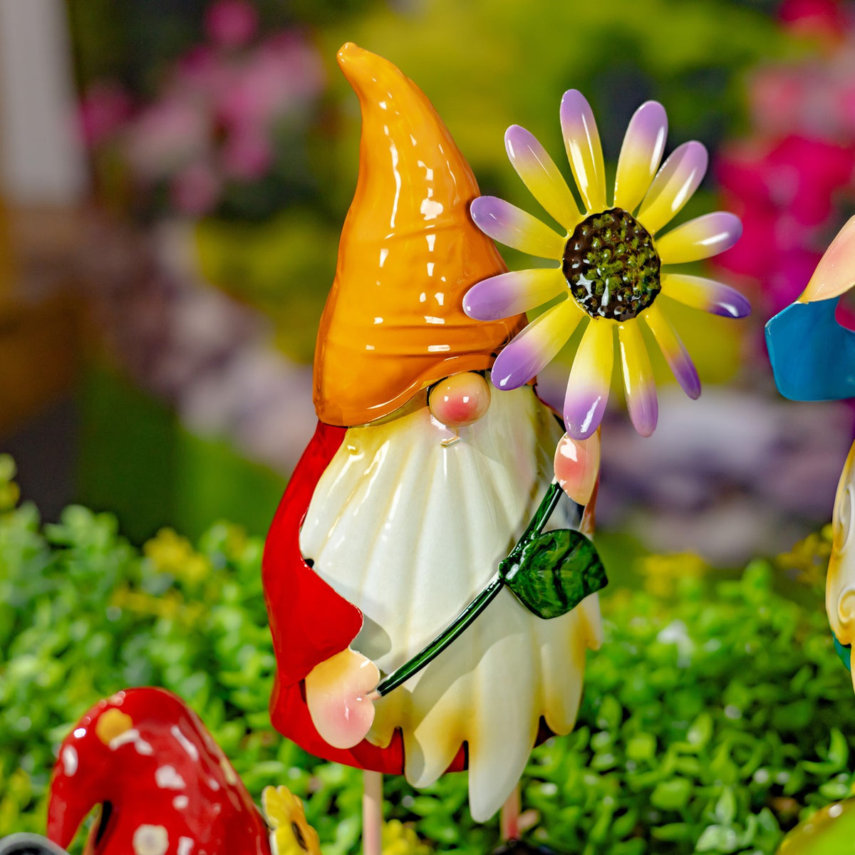 A red-clad gnome with a tall orange hat holds a purple-petaled flower in the greenery.