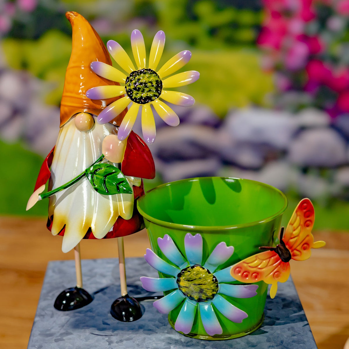 A green flower pot with a painted daisy and butterfly beside a gnome with an orange hat.
