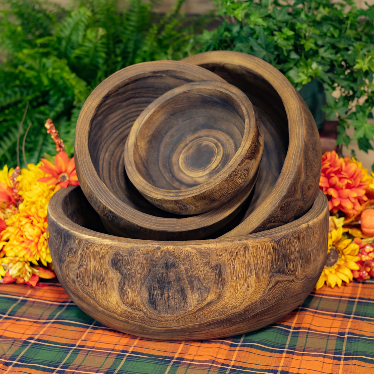 Four round wooden bowls nested together, showing their carved interiors and varied wood grain.