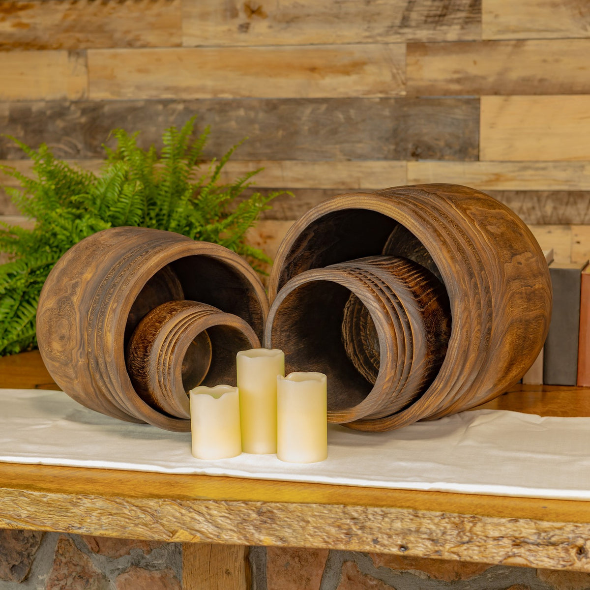 Four wooden bowls nested in two groups, with their rounded interiors facing forward beside cream candles.