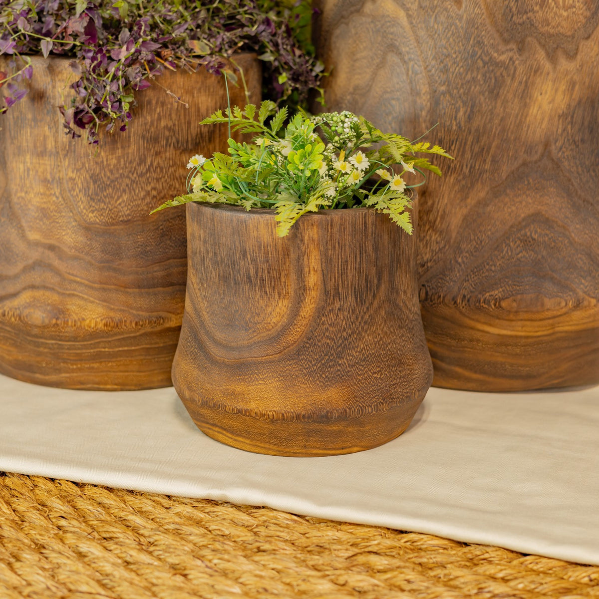 A small wooden bowl filled with greenery sits in front of two larger bowls.