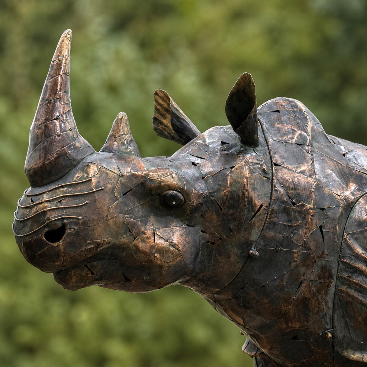 Close view of the rhinoceros statue's textured head and curved horns against greenery