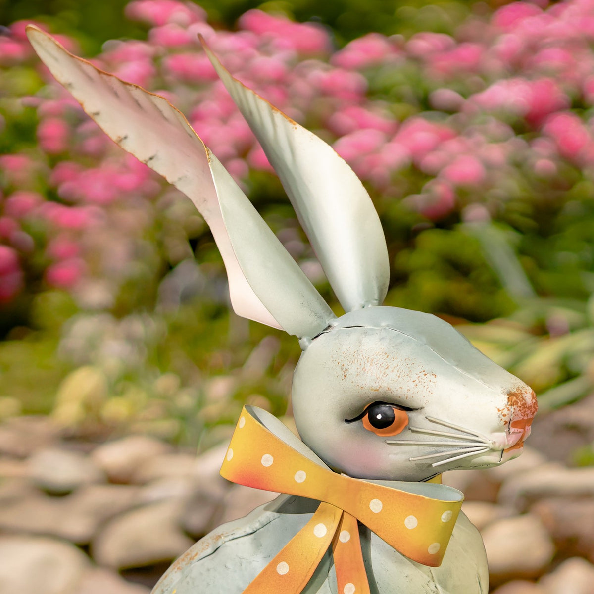 Close view of a rabbit figurine’s face, long ears, and yellow-orange dotted neck bow.